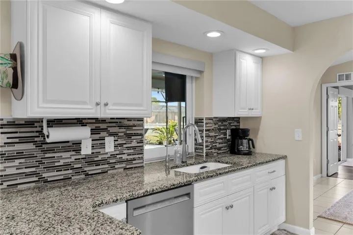 Kitchen featuring dark stone countertops, white cabinetry, dishwasher, arched walkways, and decorative backsplash