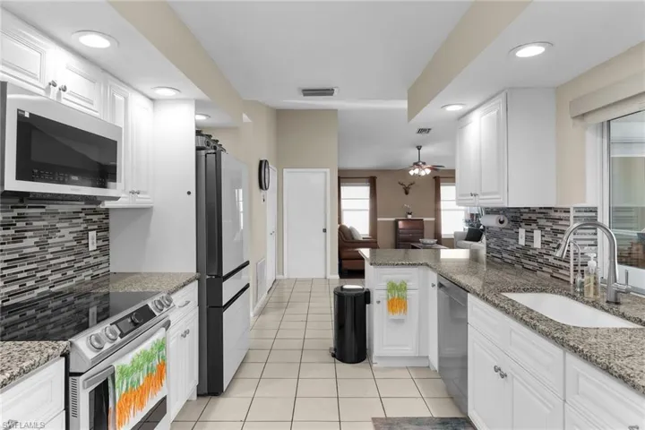 Kitchen featuring backsplash, dark stone countertops, stainless steel appliances, white cabinets, and recessed lighting