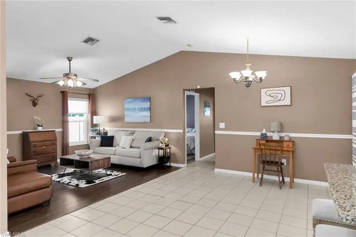 Living area with light tile patterned floors, lofted ceiling, a ceiling fan, and a chandelier