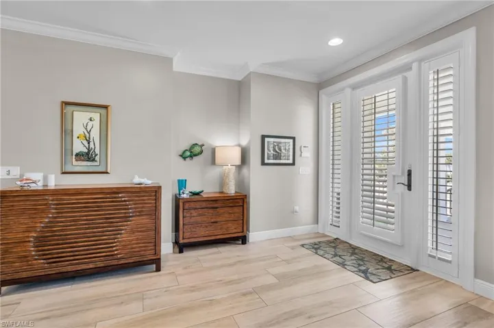 Entryway with light wood-type flooring and crown molding /  virtually enhanced photo
