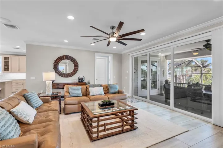 Living room featuring light wood-type flooring, crown molding, and ceiling fan /  virtually enhanced photo