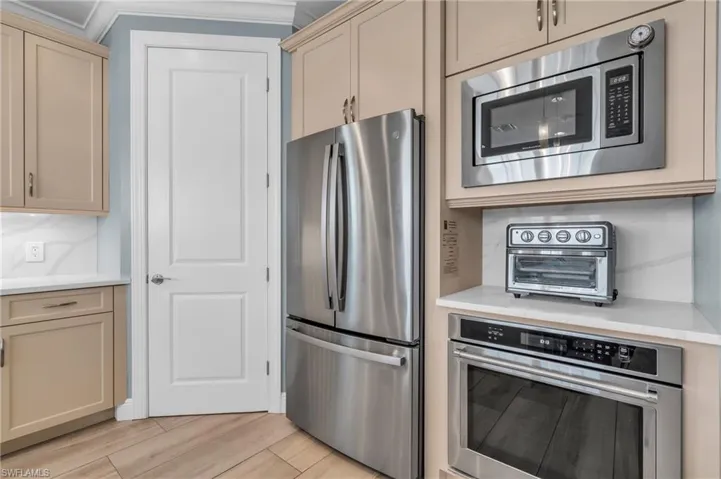 Kitchen with ornamental molding, stainless steel appliances, and light hardwood / wood-style floors /  virtually enhanced photo