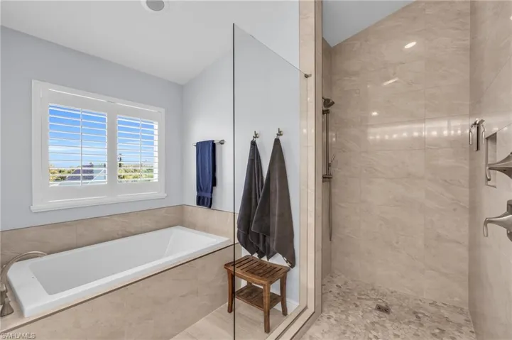 Bathroom featuring shower with separate bathtub and lofted ceiling.  virtually enhanced photo