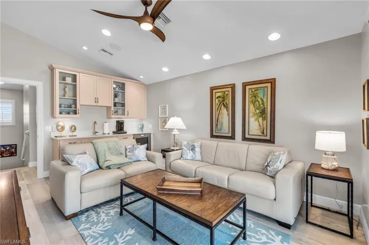 Living room featuring ceiling fan, light hardwood / wood-style floors, and vaulted ceiling /  virtually enhanced photo