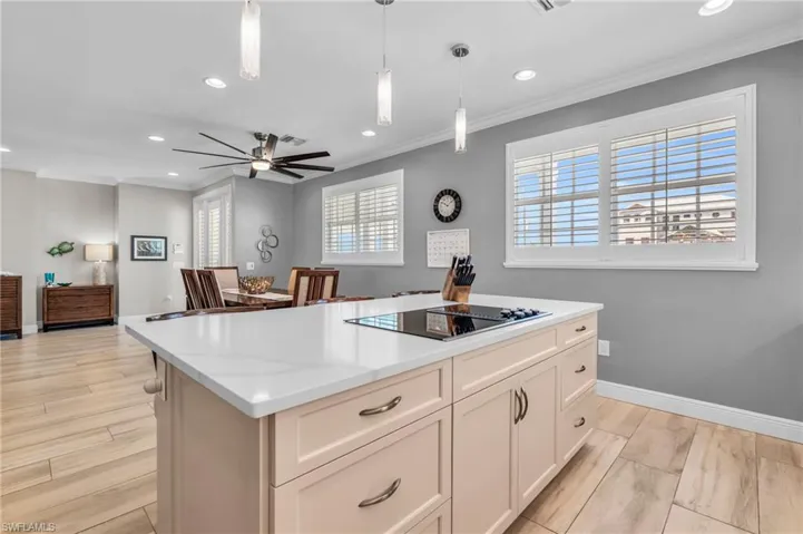 Kitchen with black electric stovetop, plenty of natural light, ceiling fan, and decorative light fixtures /  virtually enhanced photo