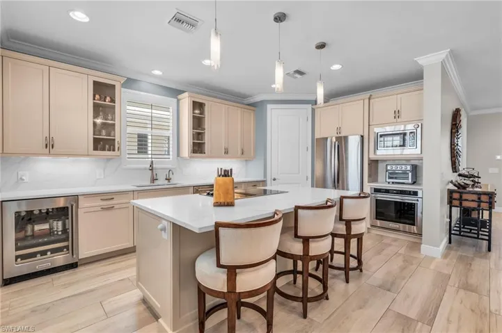 Kitchen featuring hanging light fixtures, a kitchen island, stainless steel appliances, beverage cooler, and sink /  virtually enhanced photo