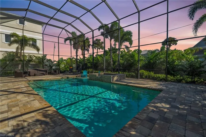 VIRTUALLY ENHANCED - Pool at dusk featuring a jacuzzi, glass enclosure, and a patio area