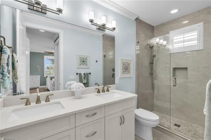 Bathroom featuring ceiling fan, vanity, an enclosed shower, crown molding, and toilet /  virtually enhanced photo