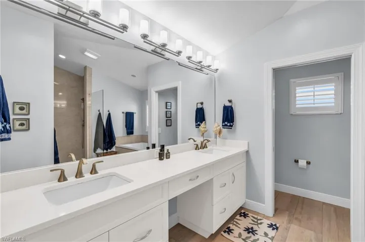 Bathroom with vanity, lofted ceiling, hardwood / wood-style floors, and tiled shower.  virtually enhanced photo