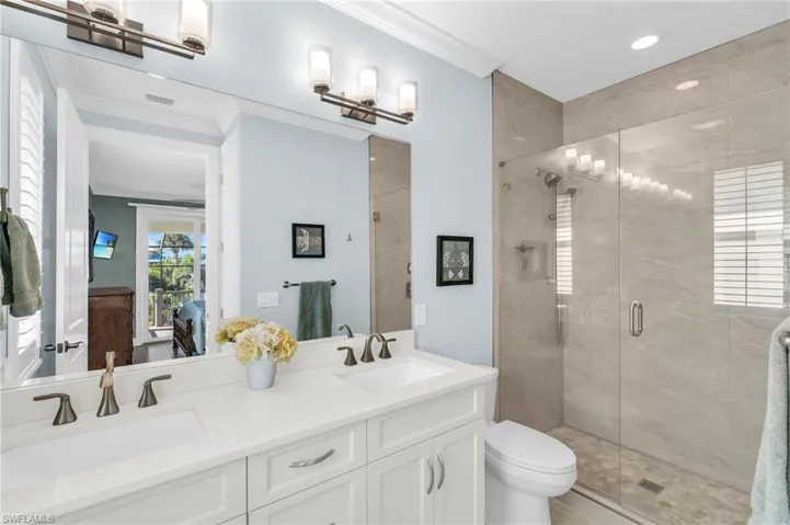 Bathroom with ornamental molding, vanity, toilet, and a shower with shower door.  virtually enhanced photo