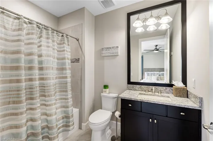 Full bathroom with vanity, shower / bath combination with curtain, toilet, and ceiling fan