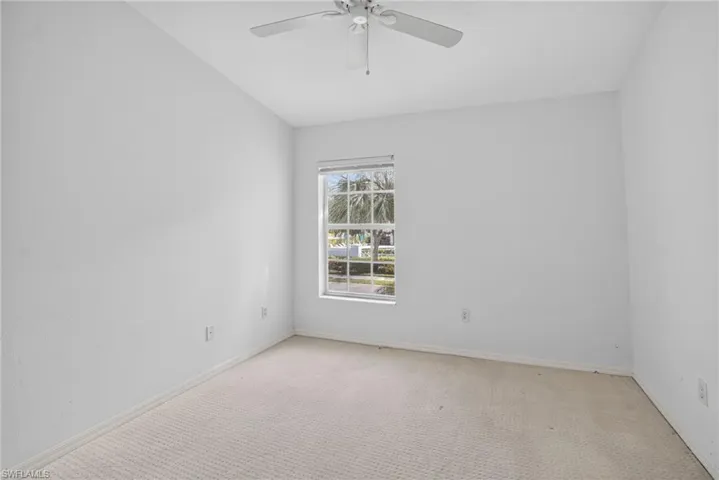 Neutral-toned room featuring a single window with white trim, a ceiling fan with integrated lighting, and light-colored carpet flooring