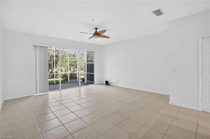 Spacious room featuring tile flooring, a ceiling fan, and sliding glass doors leading to an outdoor patio with a screened enclosure