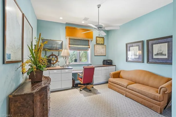 Dedicated office space featuring a window with privacy blinds, extensive built-in cabinetry, and patterned carpet flooring