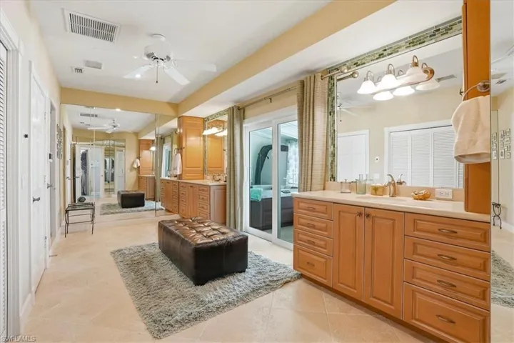 Spacious dressing area featuring tile flooring, mirrored walls, a double vanity with light wood cabinetry and a solid surface countertop, and a sliding glass door