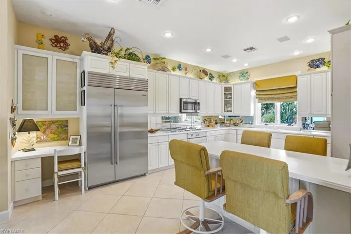 Gourmet kitchen featuring a large stainless steel refrigerator, white cabinetry, integrated desk area, tiled flooring, and recessed lighting