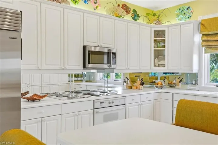 White cabinetry with decorative hardware, stainless steel appliances, a white cooktop, and a mirrored backsplash