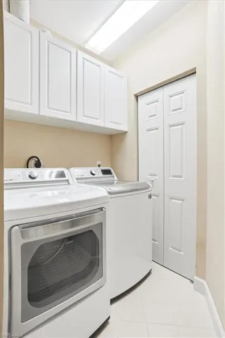 Dedicated laundry area featuring white shaker-style cabinetry, overhead fluorescent lighting, and a bi-fold pantry door