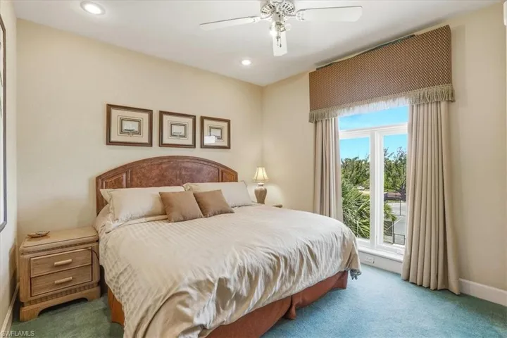 Spacious bedroom featuring recessed lighting, a ceiling fan, a large window with custom window treatments, and wall-to-wall carpeting