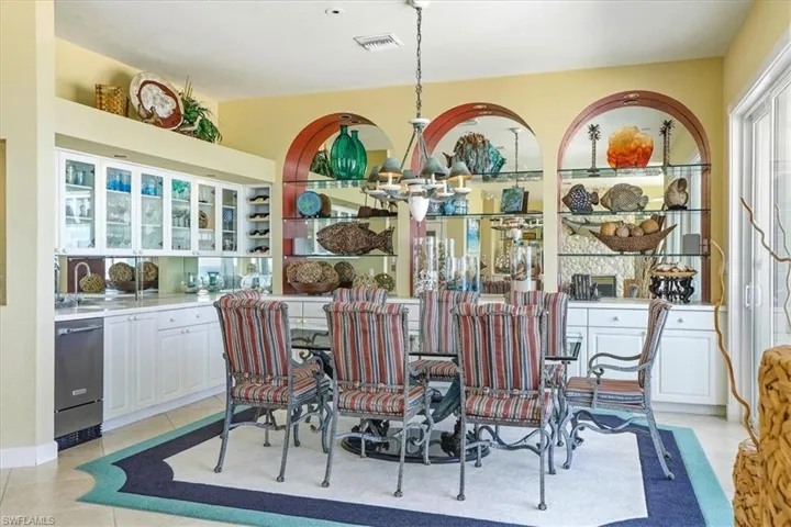 Dining area featuring a glass-top table, integrated wet bar with glass-front cabinetry, mirrored backsplash, built-in wine rack, and arched display niches with glass shelving