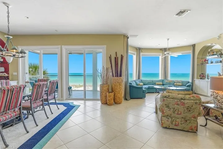 Expansive living area with large format tile flooring and multiple floor-to-ceiling glass doors and windows offering direct ocean access and waterfront scenery