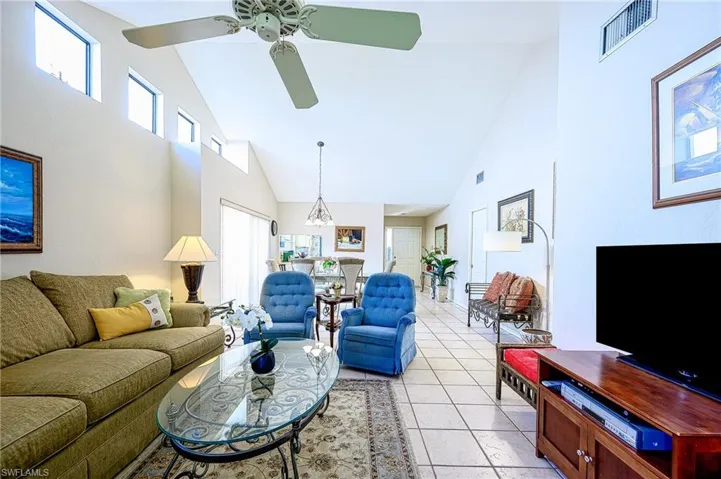 Tiled living room with high vaulted ceiling and ceiling fan with notable chandelier