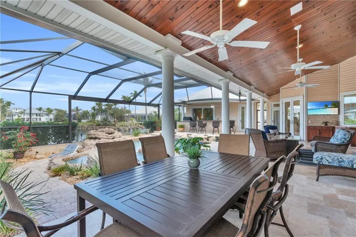 View of patio featuring a lanai, an outdoor living space, ceiling fan, a bar, and a water view