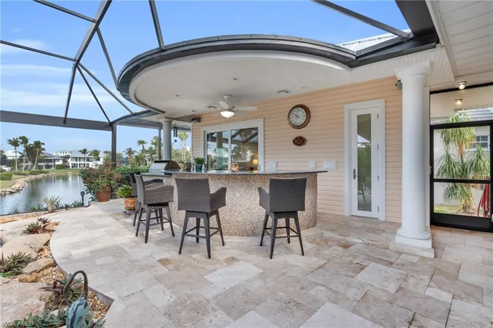 View of patio / terrace featuring exterior bar, a water view, glass enclosure, and ceiling fan