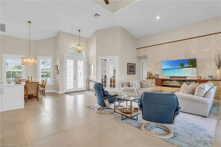 Living room with an inviting chandelier, light tile patterned flooring, high vaulted ceiling, and french doors