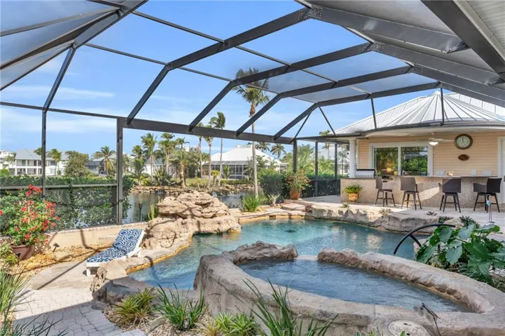 View of pool with glass enclosure, ceiling fan, a patio area, and exterior bar