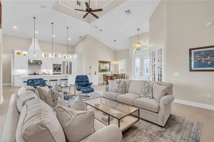 Tiled living room with ceiling fan with notable chandelier, a towering ceiling, sink, and french doors