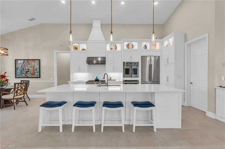 Kitchen featuring decorative light fixtures, stainless steel refrigerator, a center island with sink, and exhaust hood