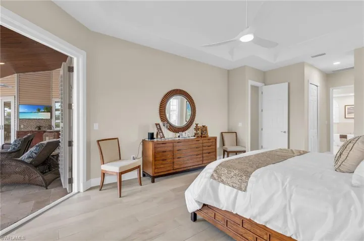 Bedroom with ensuite bath, light hardwood / wood-style floors, a raised ceiling, and ceiling fan
