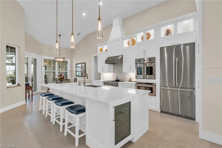 Kitchen featuring sink, an island with sink, pendant lighting, exhaust hood, and appliances with stainless steel finishes