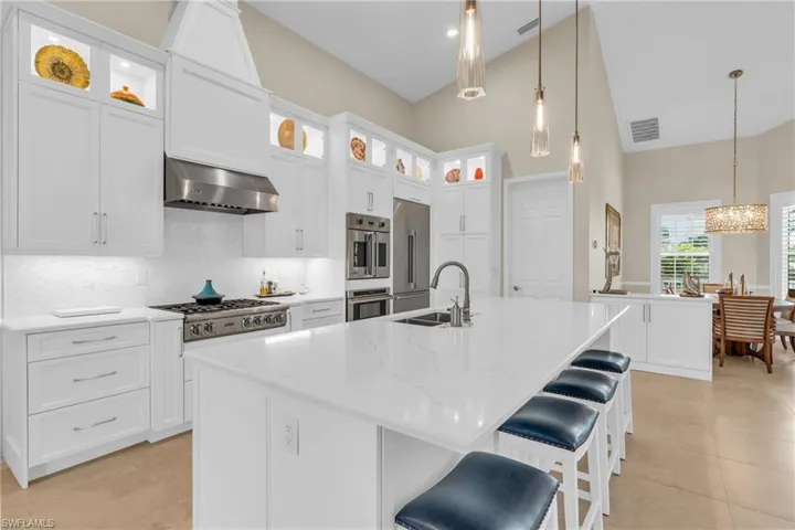 Kitchen with an island with sink, double oven, wall chimney exhaust hood, and sink