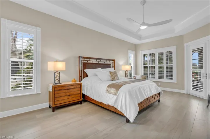 Bedroom with a raised ceiling, ceiling fan, light hardwood / wood-style floors, and access to outside