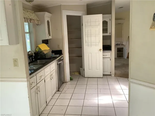 Kitchen featuring light tile patterned flooring, white cabinetry, stainless steel dishwasher, and glass insert cabinets