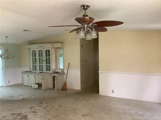 Spare room featuring a textured ceiling, vaulted ceiling, light colored carpet, a chandelier, and a ceiling fan