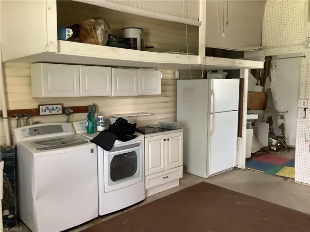 Kitchen with washing machine and dryer, freestanding refrigerator, white cabinets, and unfinished concrete flooring