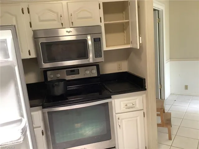 Kitchen featuring appliances with stainless steel finishes, light tile patterned flooring, dark countertops, white cabinetry, and open shelves
