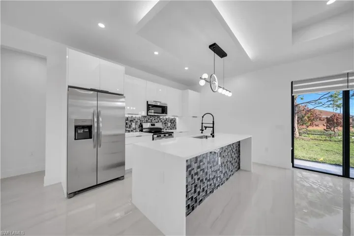 Kitchen featuring stainless steel appliances, white cabinetry, light stone counters, a kitchen island with sink, and tasteful backsplash