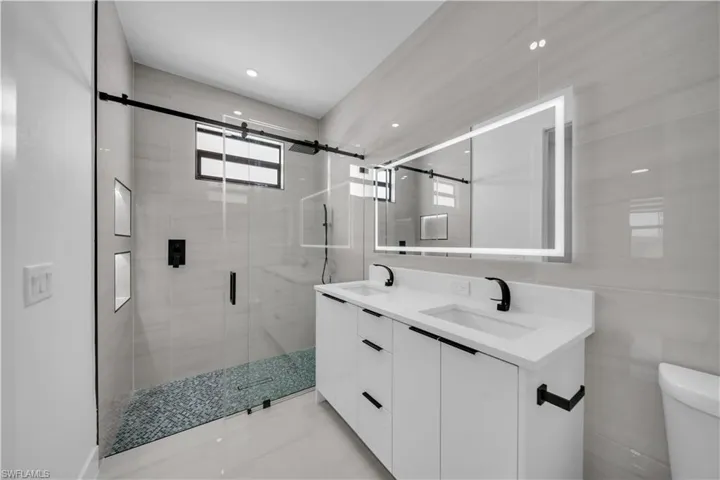 Bathroom featuring double vanity, a stall shower, tile walls, and recessed lighting