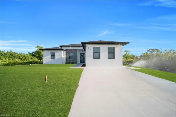 Prairie-style house with a front lawn, stone siding, concrete driveway, and stucco siding