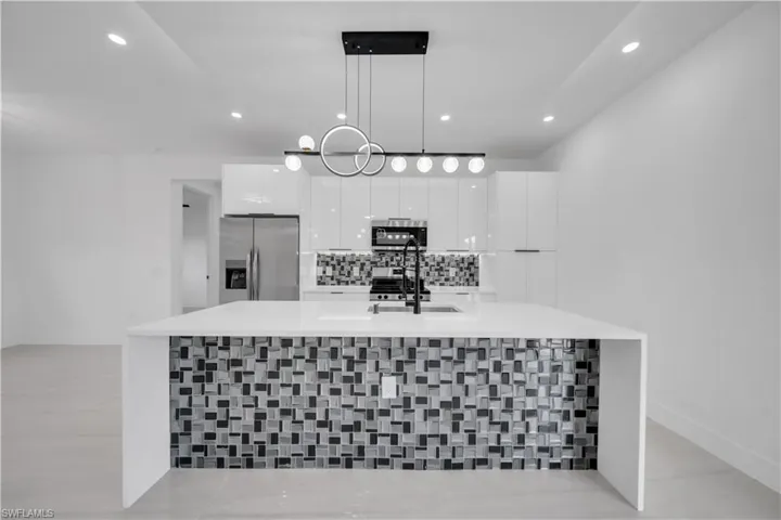 Kitchen featuring white cabinets, stainless steel appliances, decorative backsplash, a large island, and light stone countertops