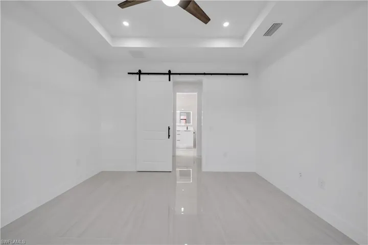 Unfurnished room featuring a barn door, ceiling fan, a raised ceiling, and recessed lighting