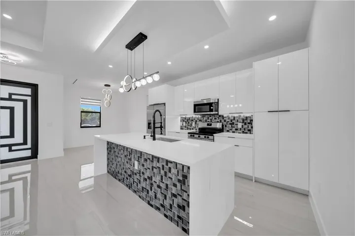 Kitchen with white cabinetry, stainless steel appliances, an island with sink, modern cabinets, and pendant lighting