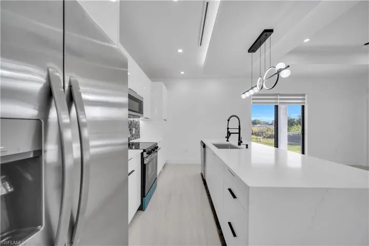 Kitchen featuring stainless steel appliances, white cabinetry, a spacious island, and light stone countertops