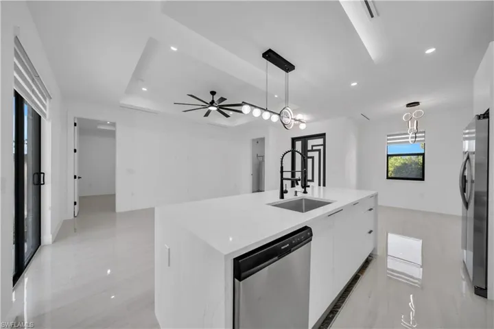 Kitchen with a center island with sink, light stone countertops, stainless steel appliances, white cabinetry, and open floor plan