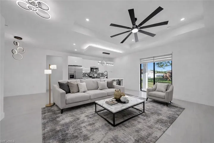 Living room with a tray ceiling, hanging lights, and ceiling fan