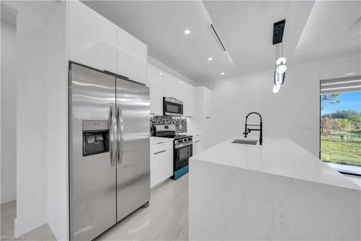 Kitchen featuring stainless steel appliances, pendant lighting, white cabinets, light stone counters, and decorative backsplash